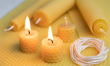 Two beeswax candles are burning, beside unlit candles and a coiled wick.