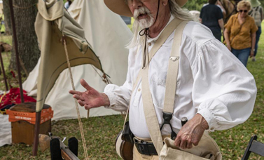 A reenactor gestures while he opens the top of his haversack.