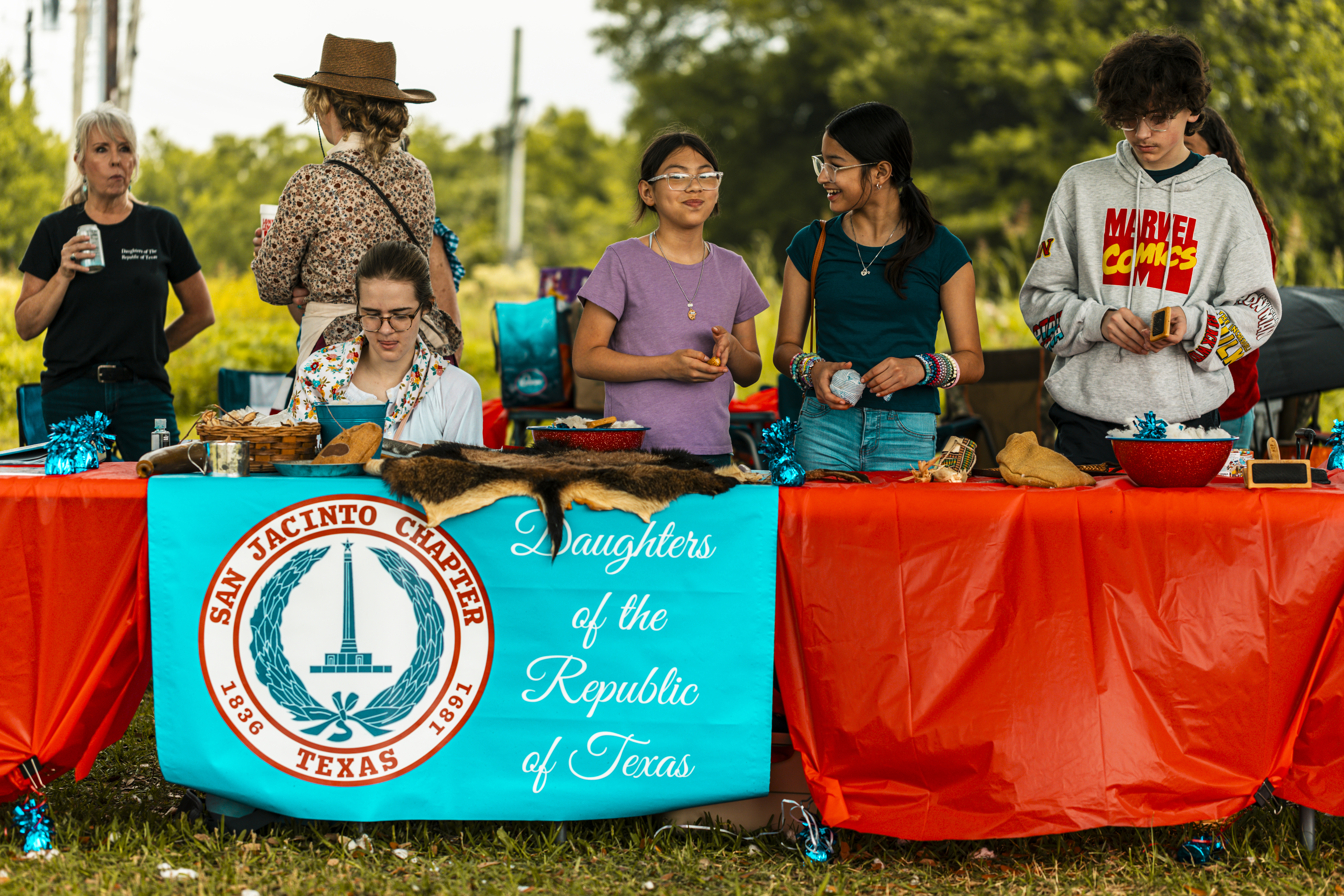 Six people stand behind a table draped with a Daughters of the Republic of Texas banner