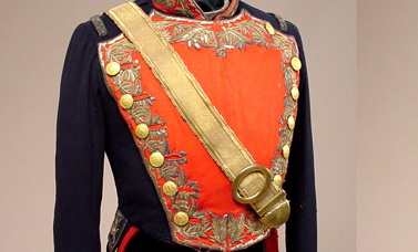 The front of a military jacket with embroidered red front, navy sleeves, and a diagonal gold belt.