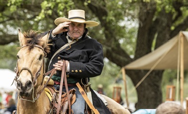 A living history re-enactor riding a horse salutes the viewer.eplica cannon.