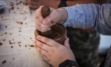 A child's hands grind something with a mortar and pestle.