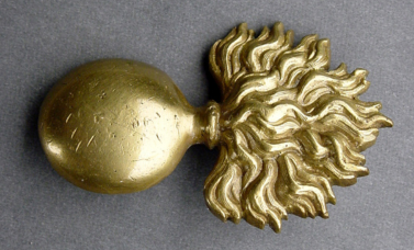 A gold-colored military insignia of an exploding bomb.