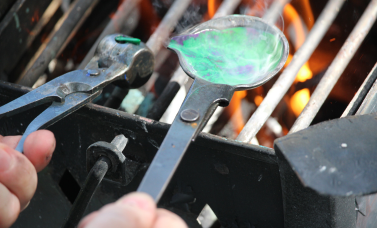 Hands hold a ladle and a bullet mold, over a fire.