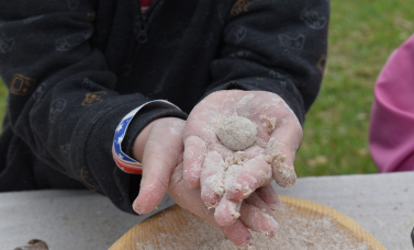 Palm-up hands with flour on them hold a ball of dough.