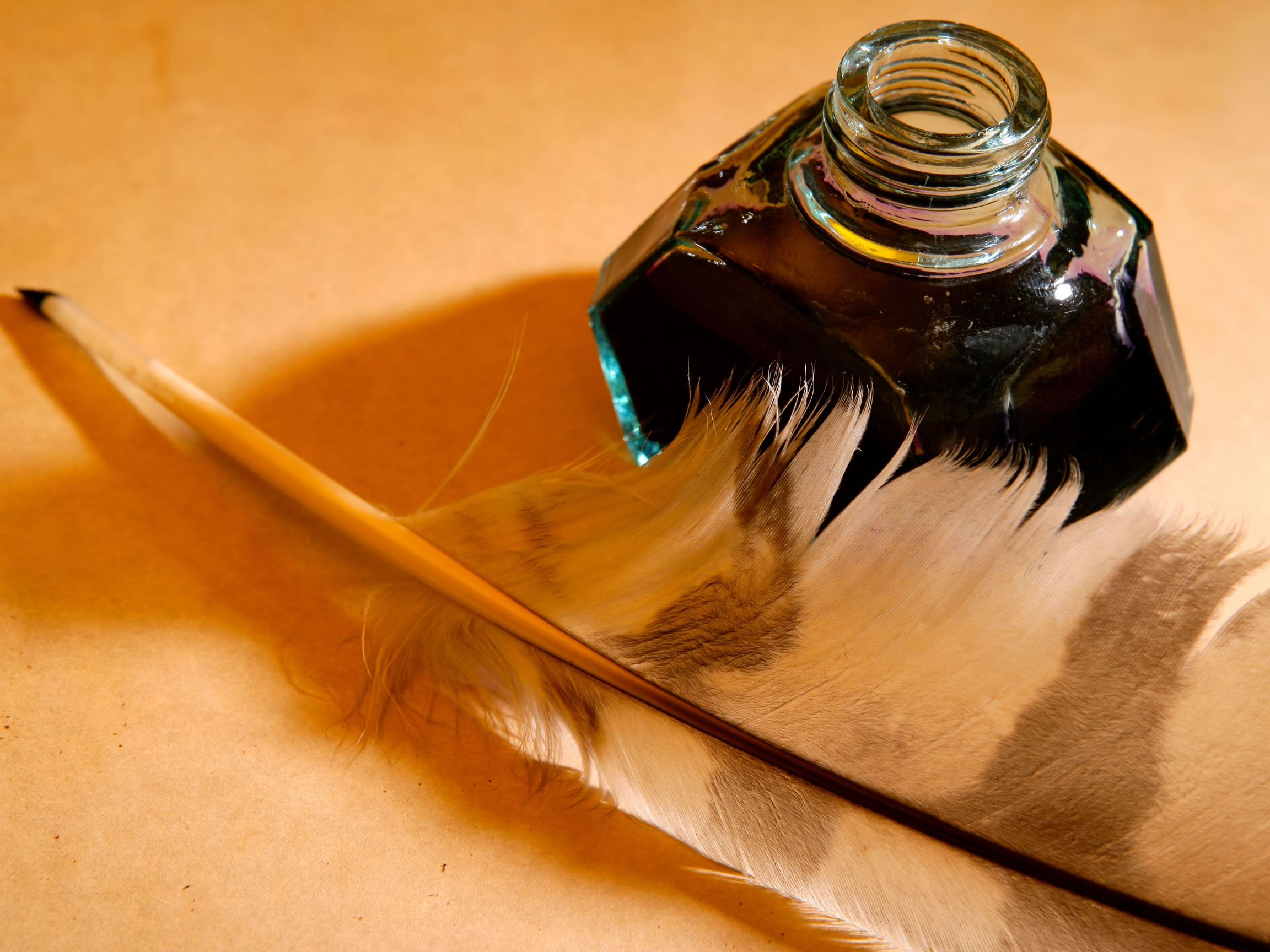 A quill pen rests by a glass bottle of ink.