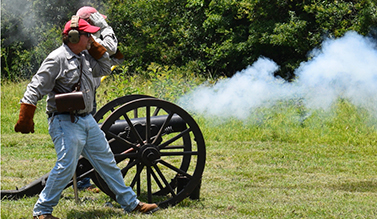 Two men cover their ears as a cannon fires.