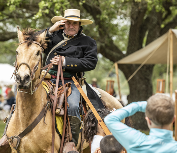 A reenactor riding a horse salutes a child who salutes back