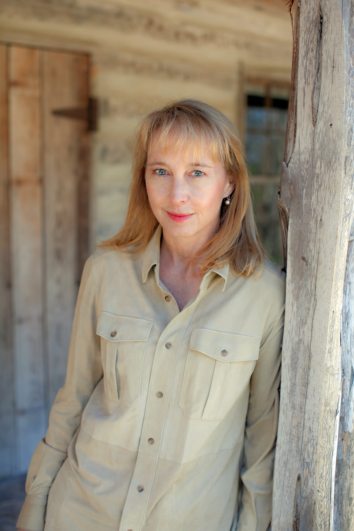 A woman leans against a post on a porch in front of a house