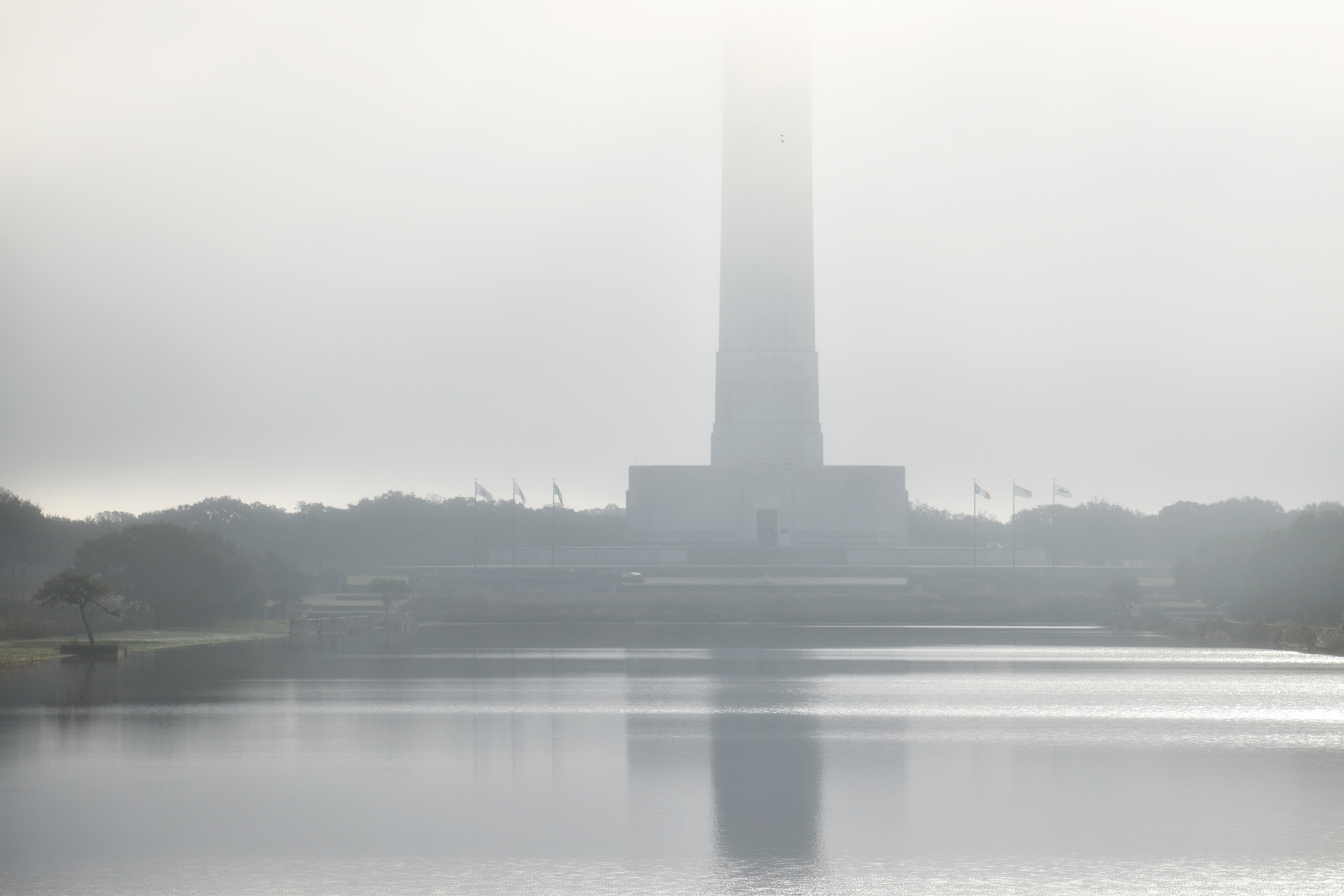 The base of the San Jacinto Monument is seen across water, through fog.