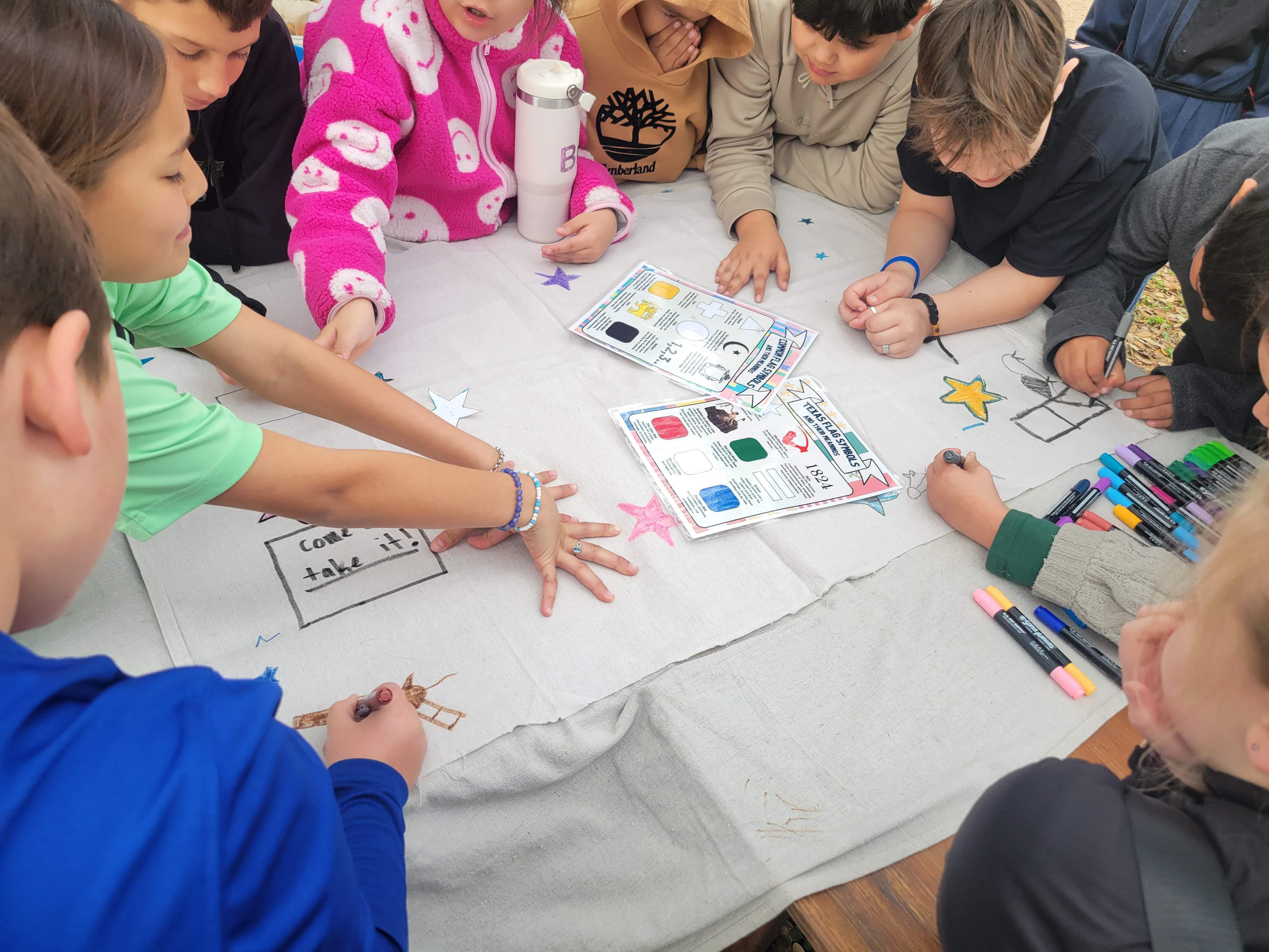 Children around a table design flags with paper and colored markers.