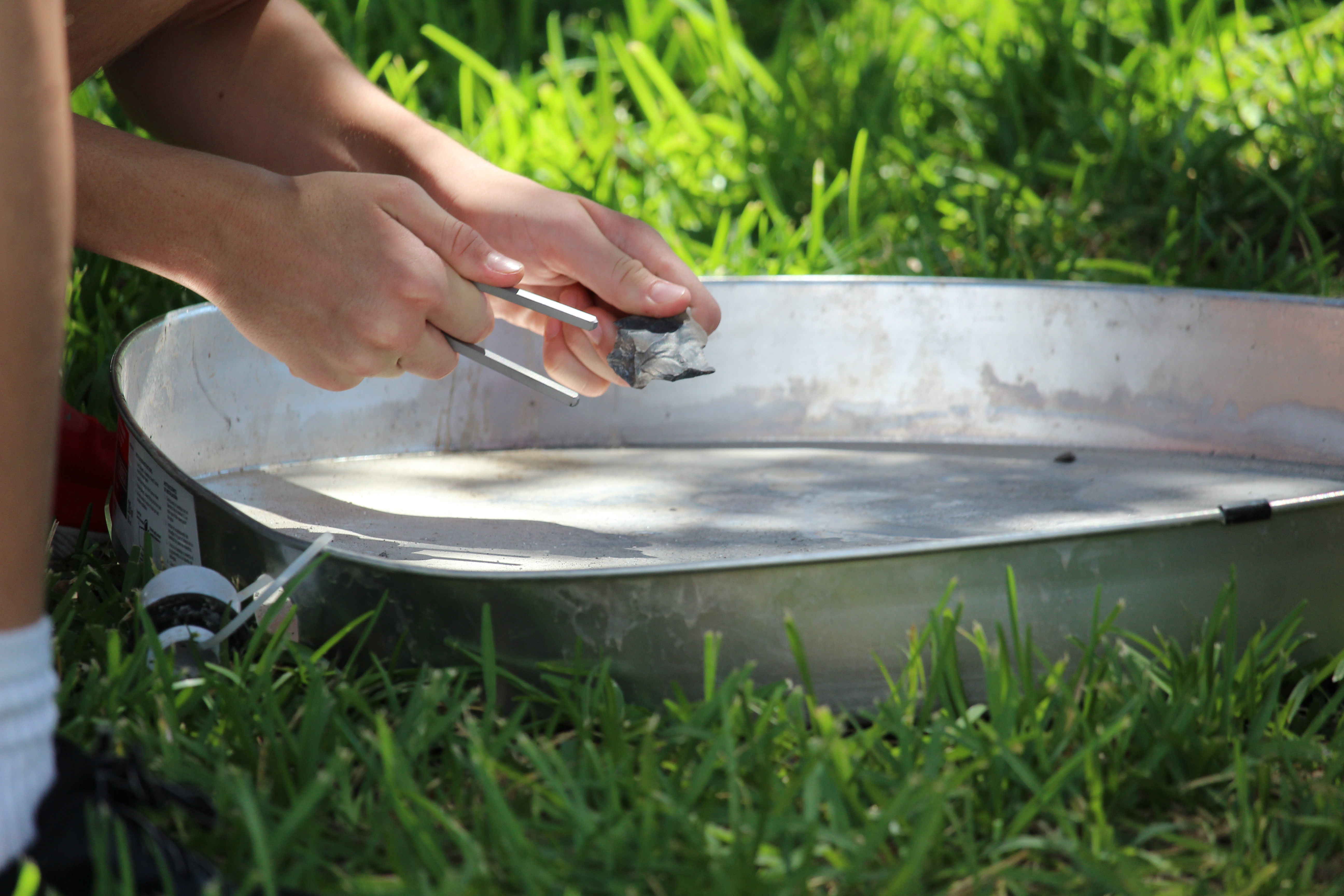 Hands hold flint near steel, over a metal container.