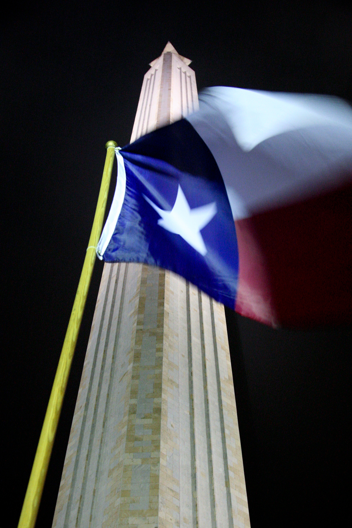 A Texas flag flies in front of the San Jacinto Monument at night.