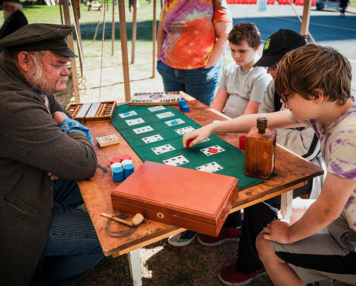 Playing cards and chips on a game table., with a reenactor and three people playing a game.