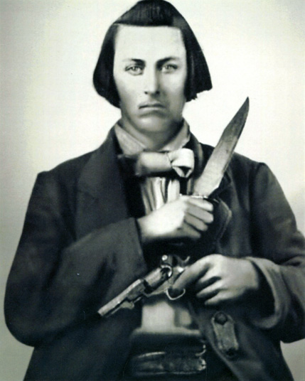 Photograph of aman holding a raised bowie knife and a gun