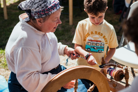 A woman shows a child how to spin.